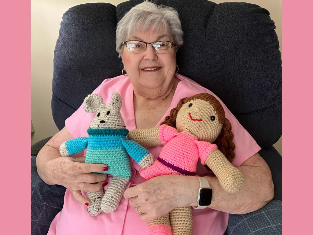 Elderly woman crocheting small stuffed dolls by hand, representing healing, purpose, and community after chiropractic care restored her mobility.