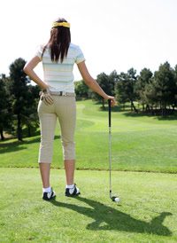 Female golfer standing on a course with one hand on her lower back, symbolizing sports-related strain and the importance of chiropractic care for athletes.