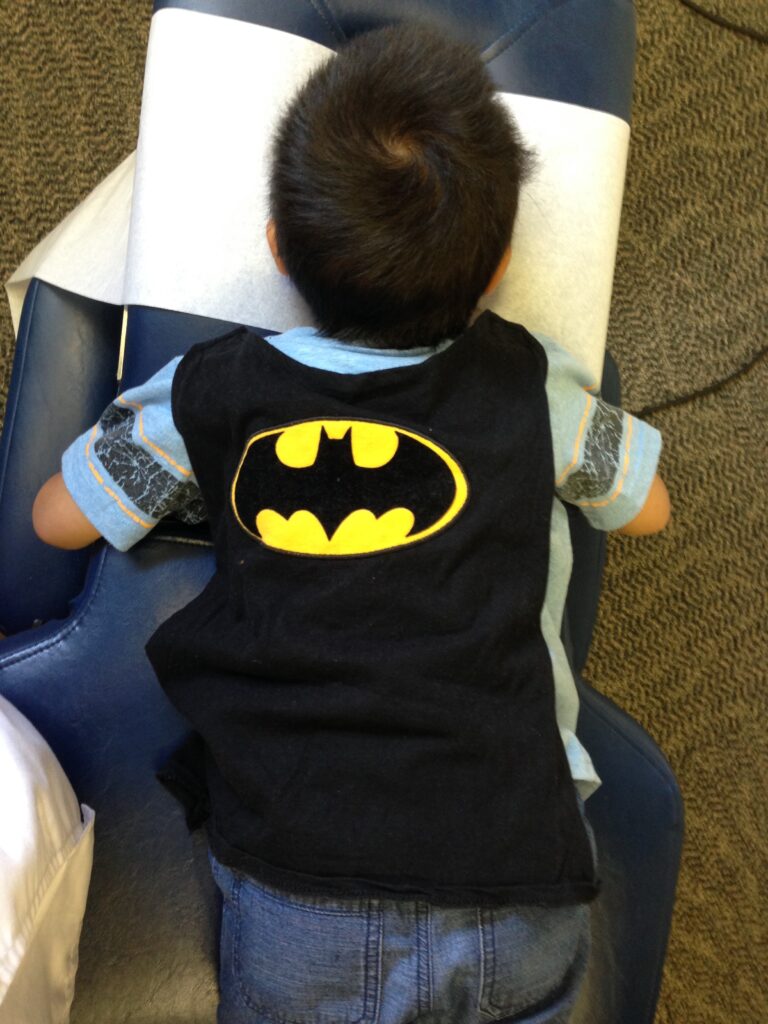 Young Thomas wearing a Batman shirt lying face down on a chiropractic adjusting table during Superhero Camp.