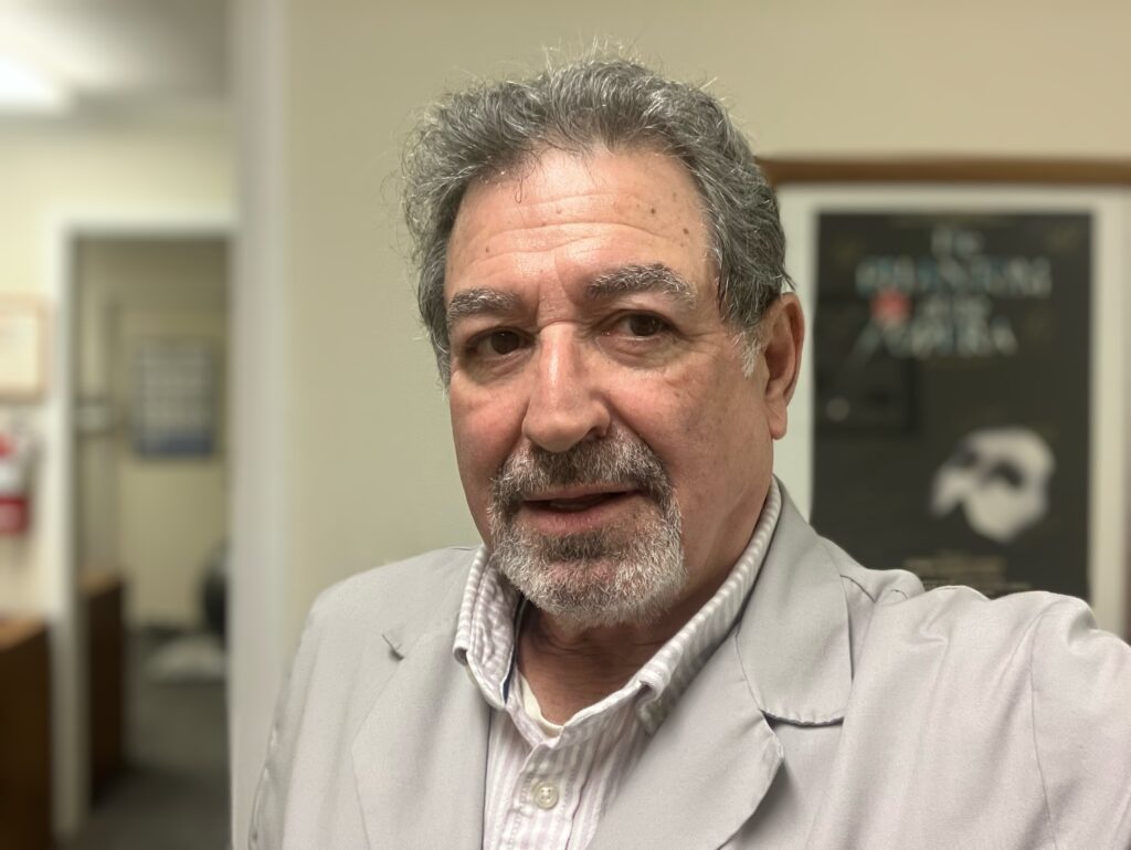 Dr. Steve Segal, Libertyville chiropractor, smiling in office with Phantom of the Opera poster behind him